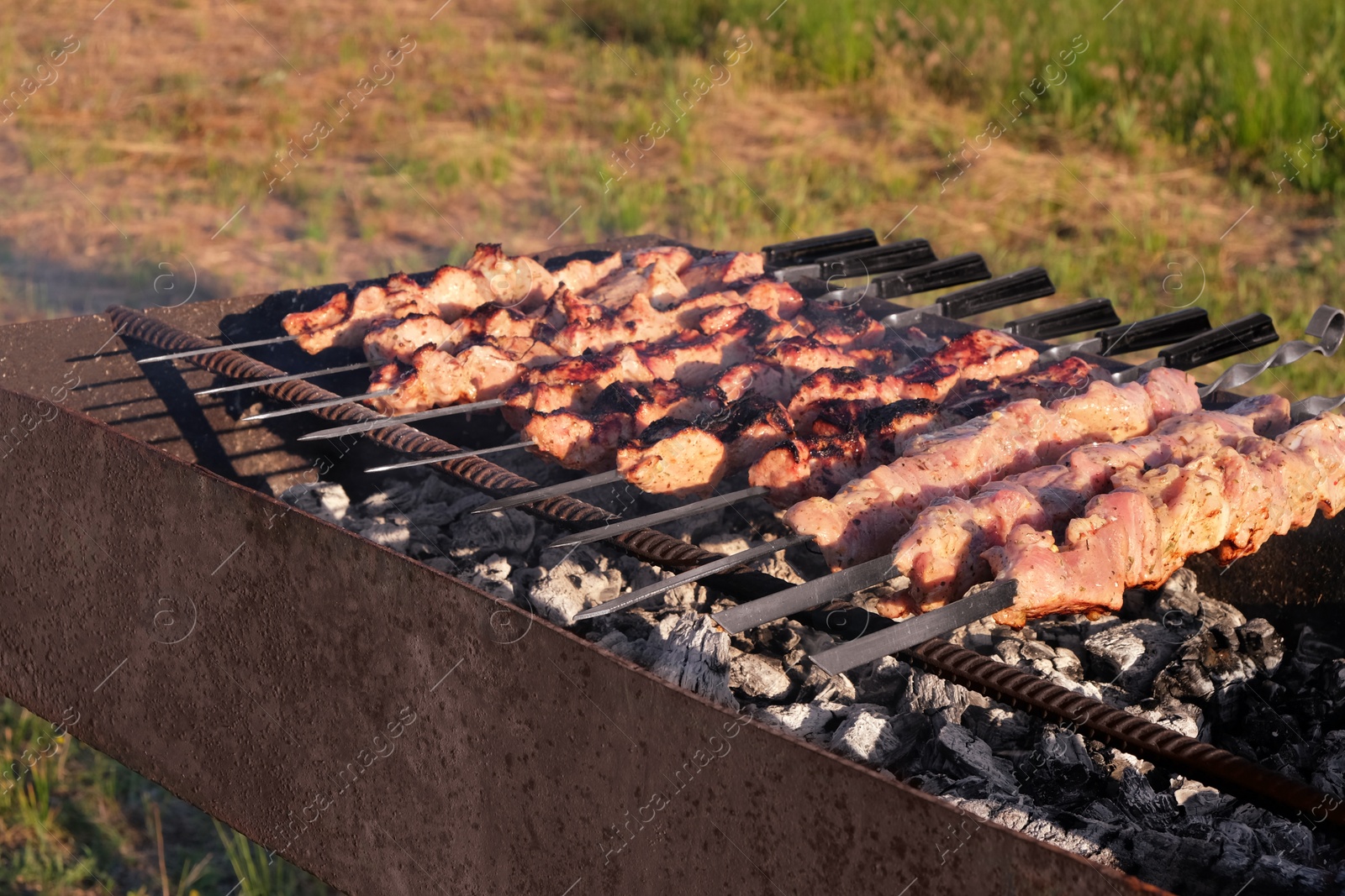 Cooking tasty kebab on metal skewers outdoors Photo of Cooking tasty kebab on metal skewers outdoors