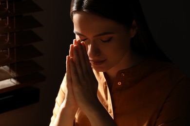 Religious young woman with clasped hands praying indoors, closeup Photo of Religious young woman with clasped hands praying indoors, closeup