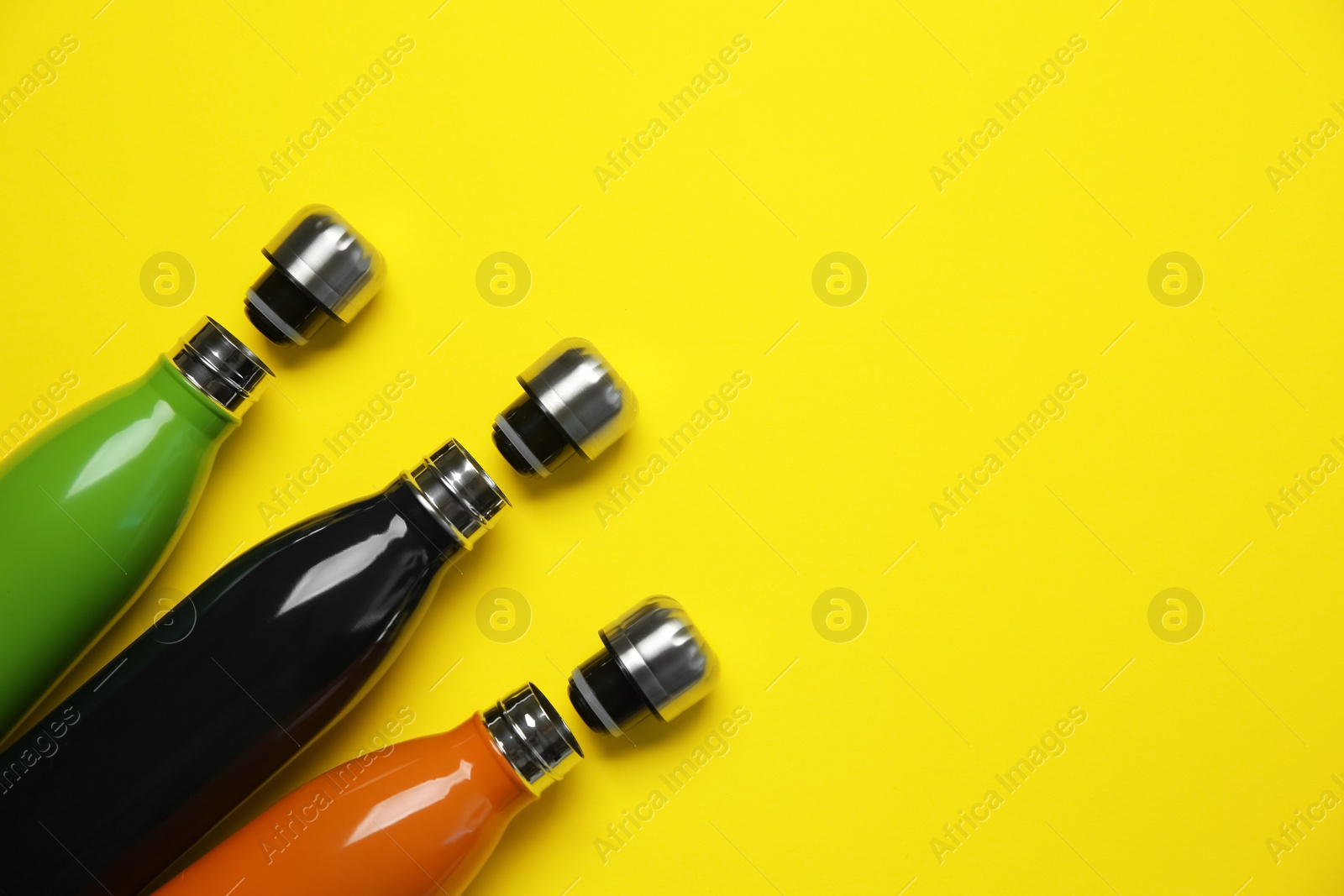 Different thermo bottles on yellow background, flat lay. Space for text Photo of Different thermo bottles on yellow background, flat lay. Space for text