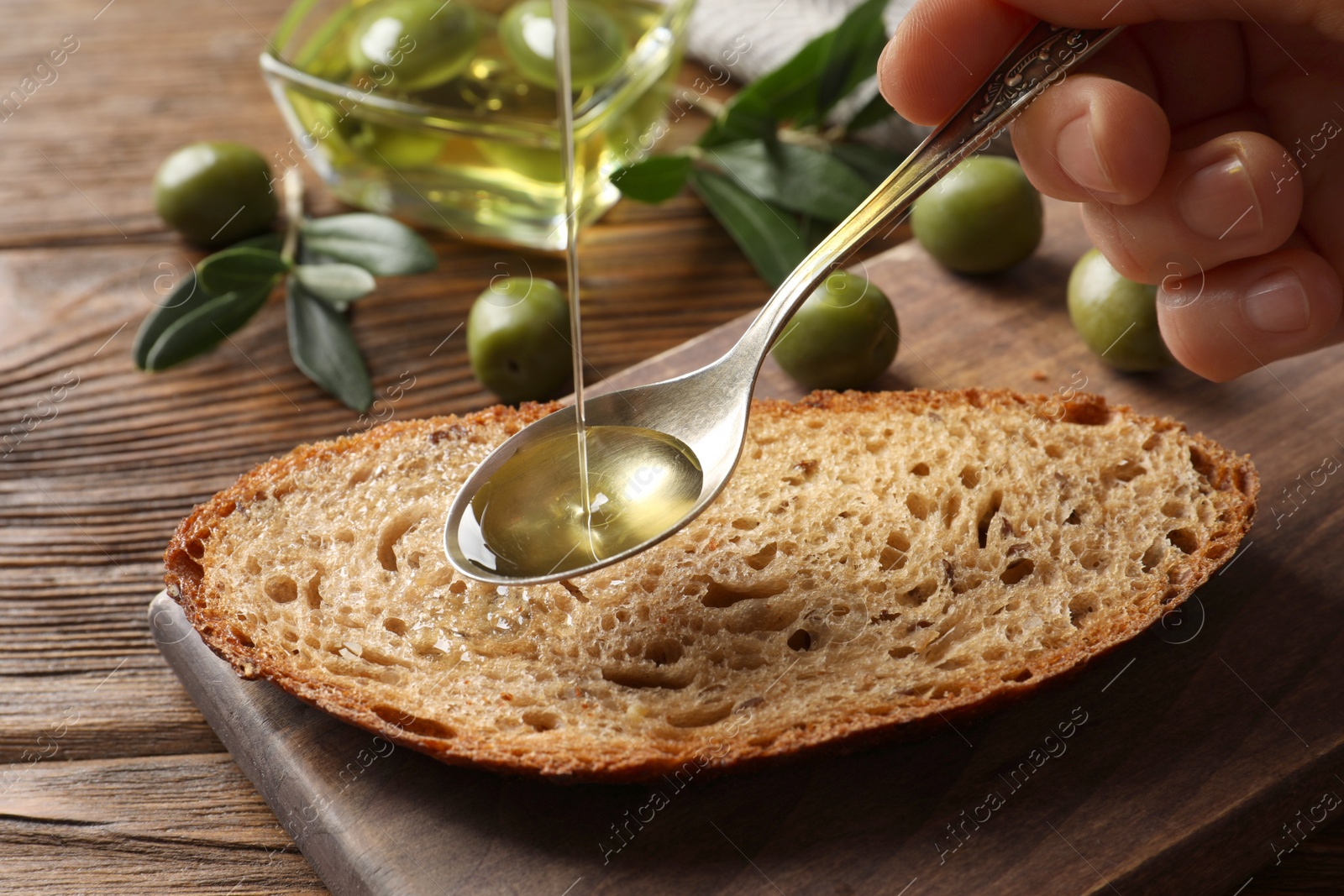 Woman pouring olive oil into spoon over bread at wooden table, closeup Photo of Woman pouring olive oil into spoon over bread at wooden table, closeup