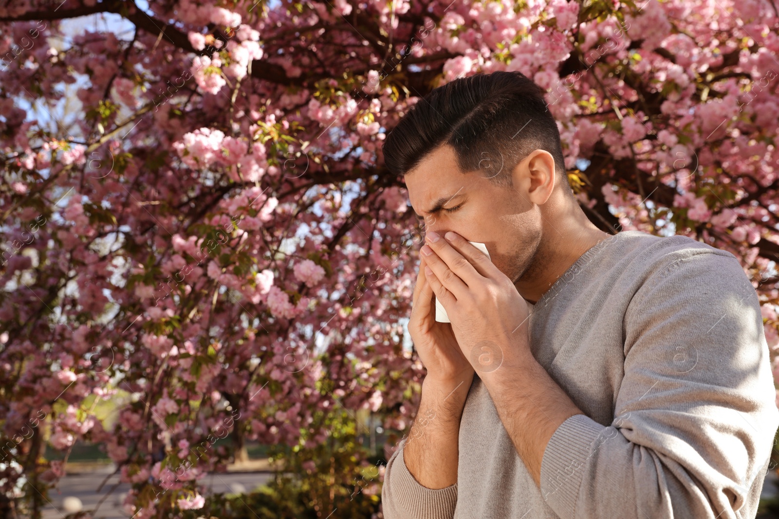 Man suffering from seasonal pollen allergy near blossoming tree outdoors Photo of Man suffering from seasonal pollen allergy near blossoming tree outdoors