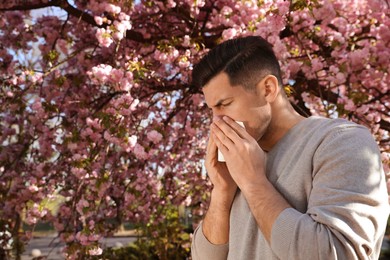 Man suffering from seasonal pollen allergy near blossoming tree outdoors Photo of Man suffering from seasonal pollen allergy near blossoming tree outdoors