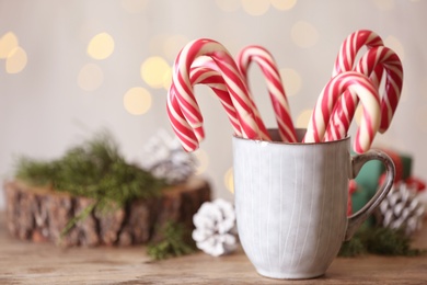 Christmas candy canes in cup on wooden table against blurred lights, space for text Photo of Christmas candy canes in cup on wooden table against blurred lights, space for text
