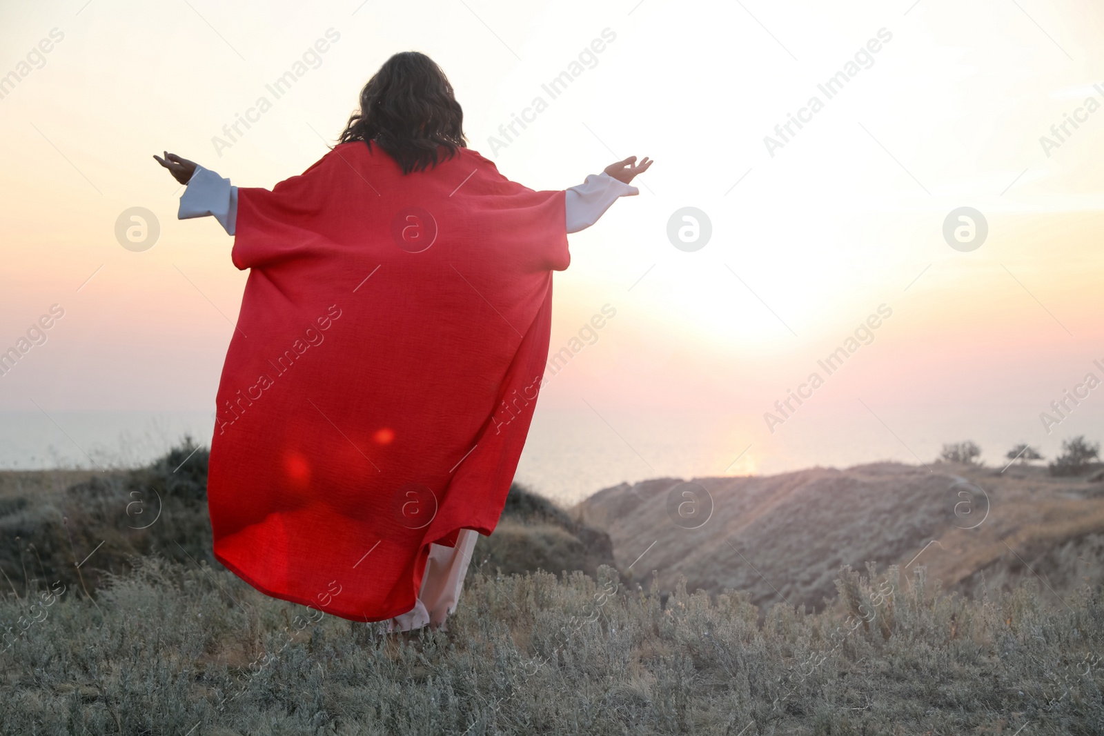 Jesus Christ raising hands on hills at sunset, back view. Space for text Photo of Jesus Christ raising hands on hills at sunset, back view. Space for text