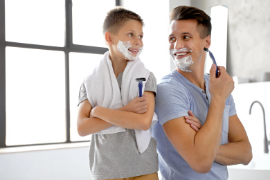 Happy father and son with shaving foam on their faces in bathroom Photo of Happy father and son with shaving foam on their faces in bathroom