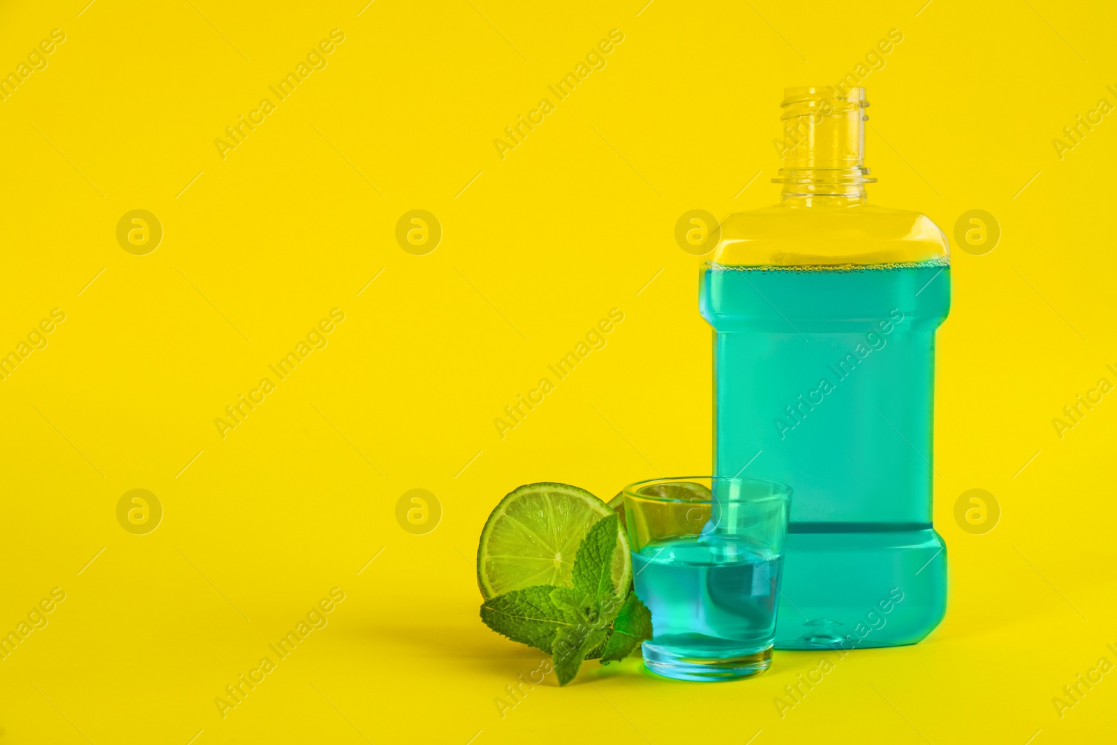 Mouthwash, fresh mint and lime on yellow background. Space for text Photo of Mouthwash, fresh mint and lime on yellow background. Space for text