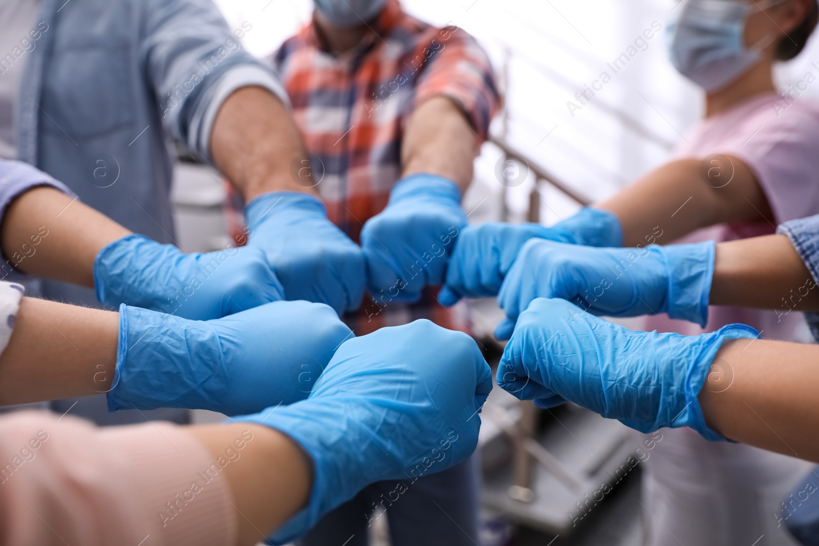 People in blue medical gloves joining fists indoors, closeup Photo of People in blue medical gloves joining fists indoors, closeup
