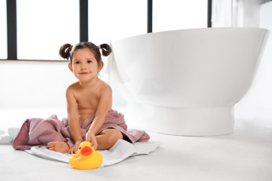 Photo of Cute little girl near tub in bathroom. Space for text
