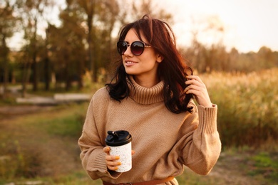 Photo of Beautiful young woman with cup of coffee wearing stylish autumn sweater outdoors
