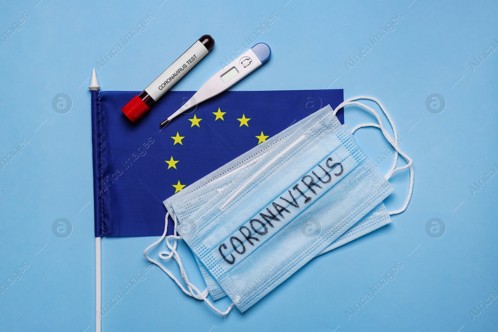 European Union flag, protective masks, thermometer and test tube with blood sample on light blue background, flat lay. Coronavirus outbreak Photo of European Union flag, protective masks, thermometer and test tube with blood sample on light blue background, flat lay. Coronavirus outbreak