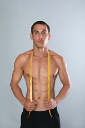 Handsome shirtless man with slim body and measuring tape on grey background Photo of Handsome shirtless man with slim body and measuring tape on grey background