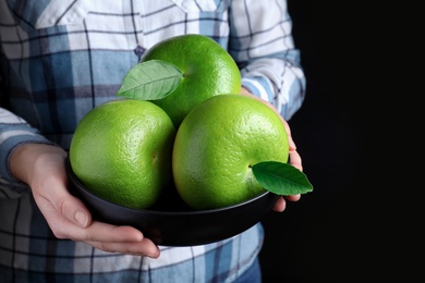 Woman holding bowl with sweetie fruits on black background, closeup Photo of Woman holding bowl with sweetie fruits on black background, closeup