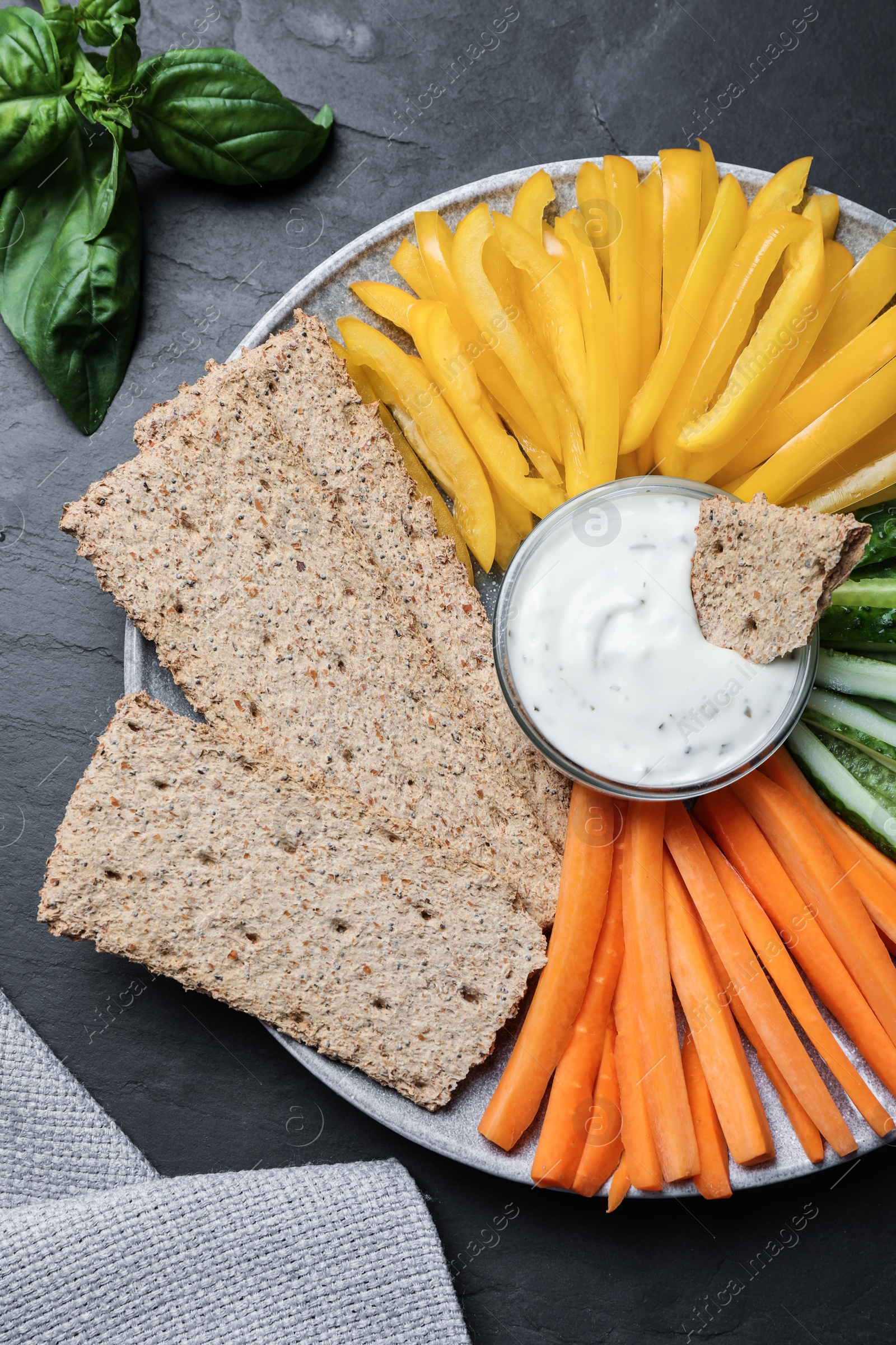 Plate with crispbreads, vegetable sticks and dip sauce on black table, top view Photo of Plate with crispbreads, vegetable sticks and dip sauce on black table, top view