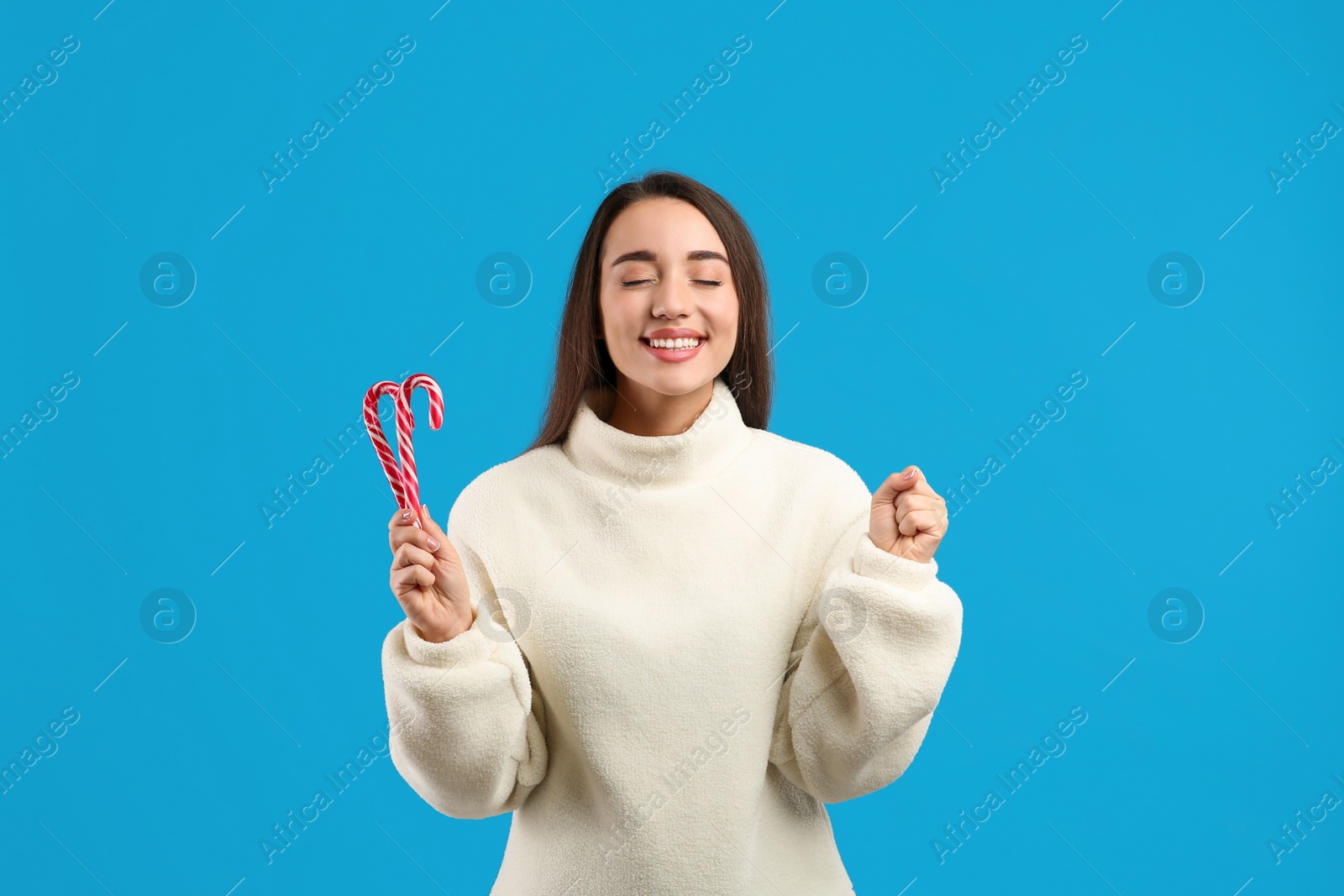 Young woman in beige sweater holding candy canes on blue background. Celebrating Christmas Photo of Young woman in beige sweater holding candy canes on blue background. Celebrating Christmas