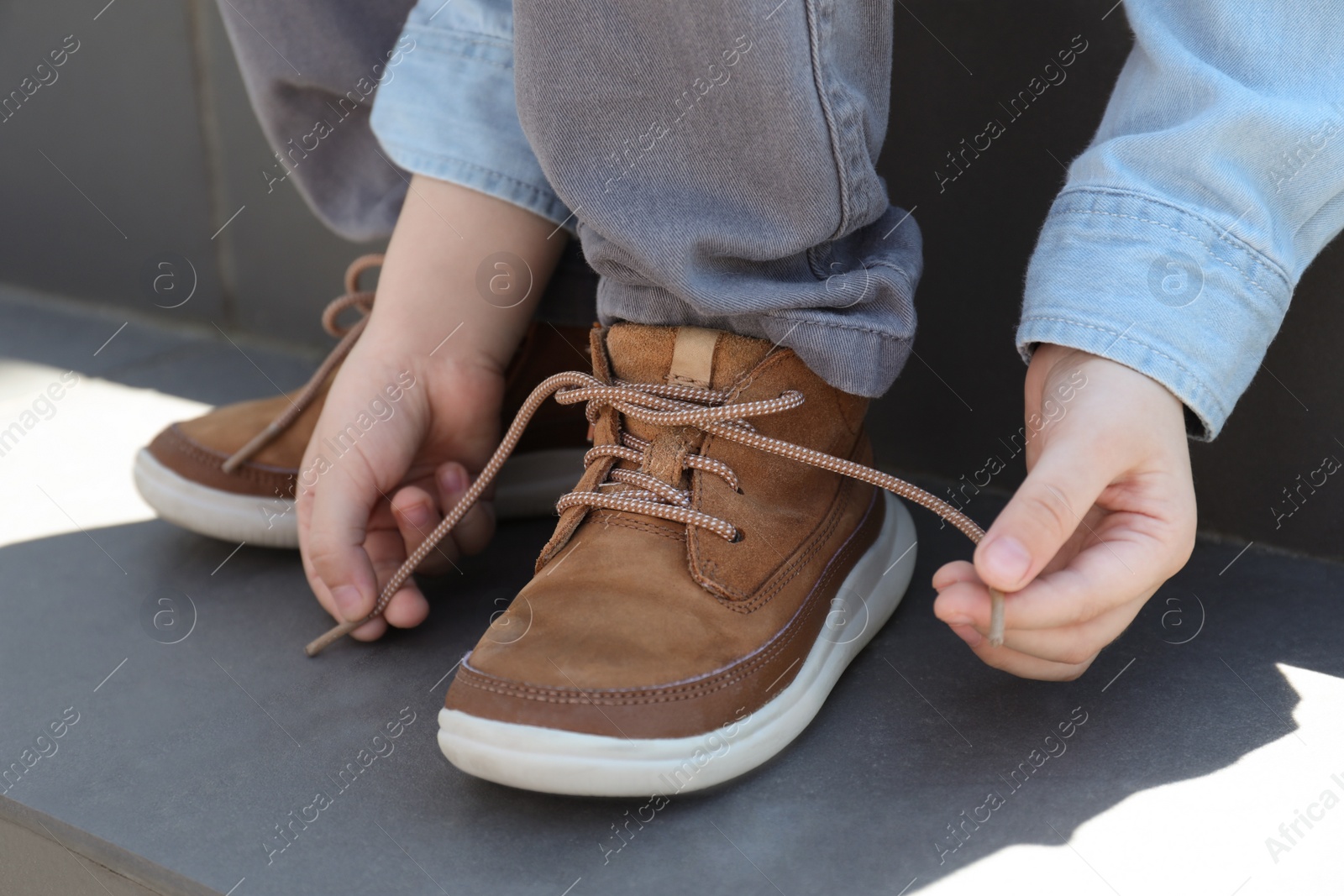 Little boy tying shoe laces on stairs outdoors, closeup Photo of Little boy tying shoe laces on stairs outdoors, closeup