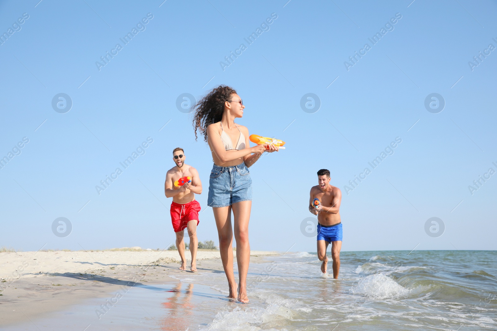 Friends with water guns having fun on beach Photo of Friends with water guns having fun on beach