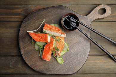 Fresh crab sticks with cucumber and soy sauce served on wooden table, flat lay Photo of Fresh crab sticks with cucumber and soy sauce served on wooden table, flat lay