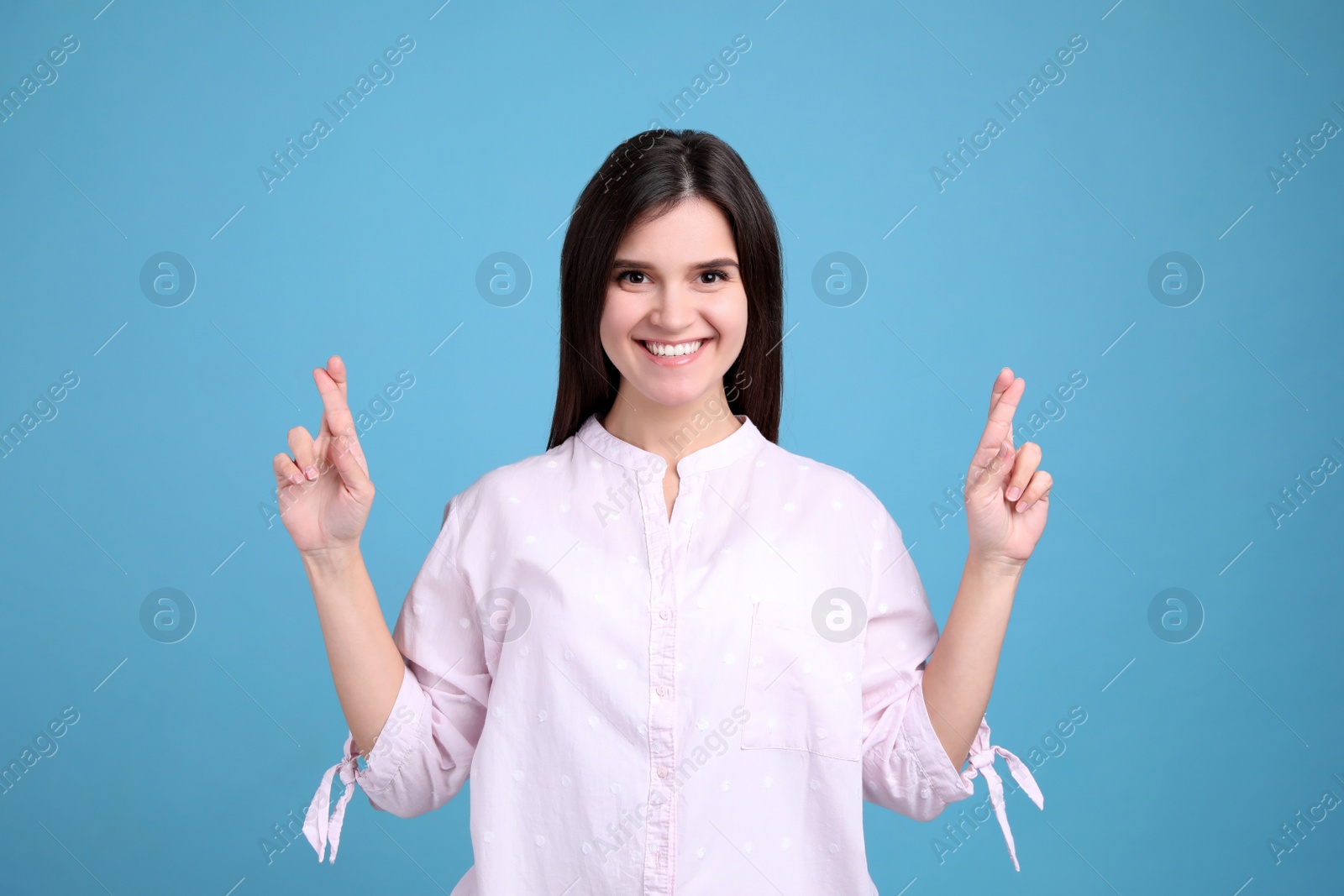 Happy young woman crossing fingers on light blue background. Dealing with stress Photo of Happy young woman crossing fingers on light blue background. Dealing with stress