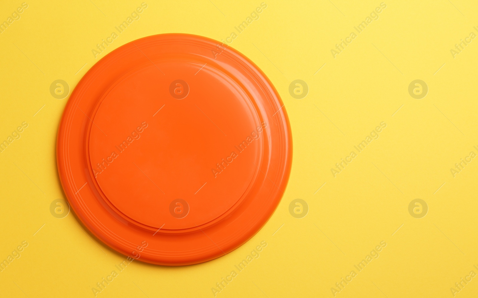 Orange plastic frisbee disk on yellow background, top view. Space for text Photo of Orange plastic frisbee disk on yellow background, top view. Space for text