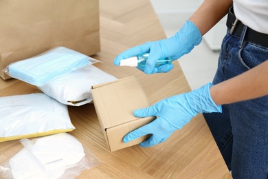 Woman spraying antiseptic onto parcel at wooden table, closeup. Preventive measure during COVID-19 pandemic Photo of Woman spraying antiseptic onto parcel at wooden table, closeup. Preventive measure during COVID-19 pandemic