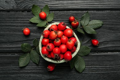 Ripe rose hip berries with green leaves on black wooden table, flat lay Photo of Ripe rose hip berries with green leaves on black wooden table, flat lay