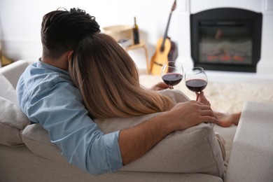 Couple with glasses of wine resting on sofa near fireplace at home, back view Photo of Couple with glasses of wine resting on sofa near fireplace at home, back view