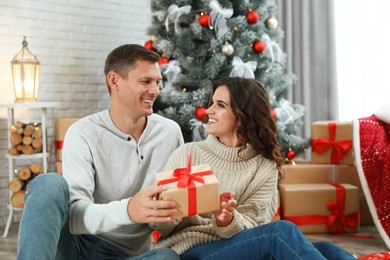 Man presenting Christmas gift to his girlfriend at home Image of Man presenting Christmas gift to his girlfriend at home