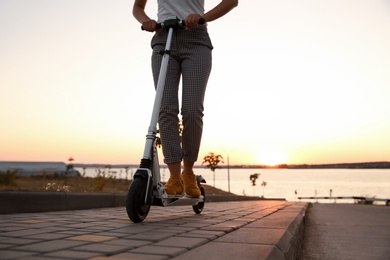 Woman riding electric kick scooter outdoors at sunset, closeup Photo of Woman riding electric kick scooter outdoors at sunset, closeup