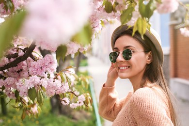 Happy stylish young woman near blossoming sakura tree outdoors. Spring look Photo of Happy stylish young woman near blossoming sakura tree outdoors. Spring look