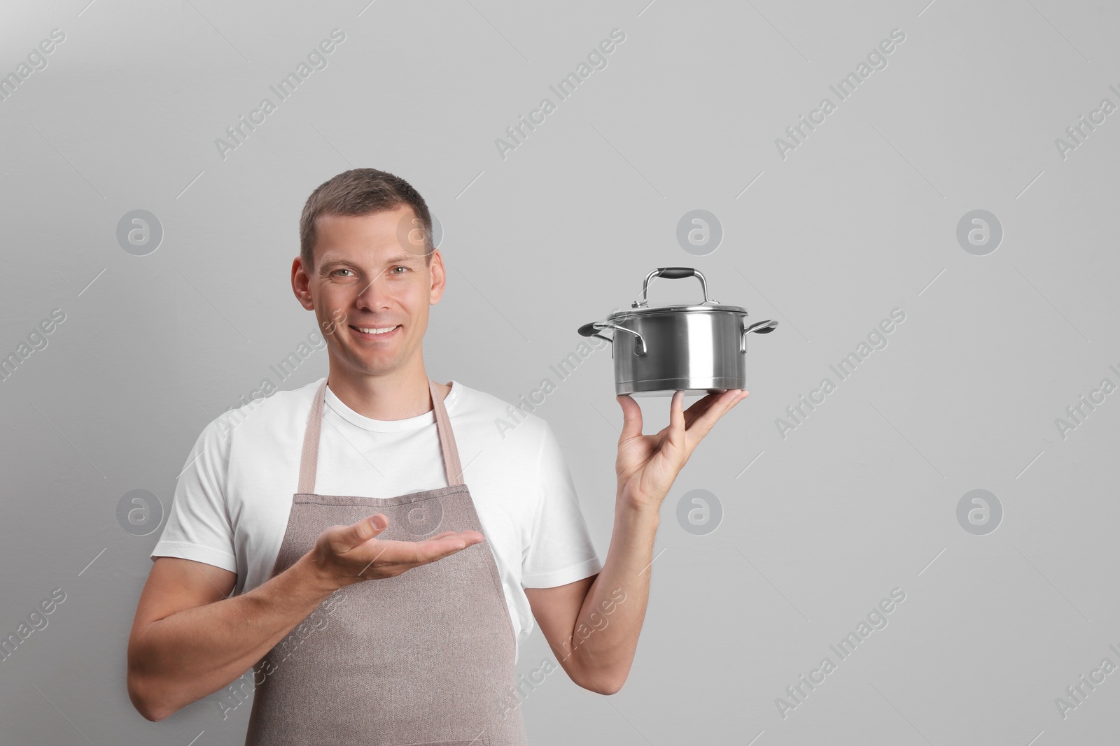 Happy man with cooking pot on light grey background. Space for text Photo of Happy man with cooking pot on light grey background. Space for text