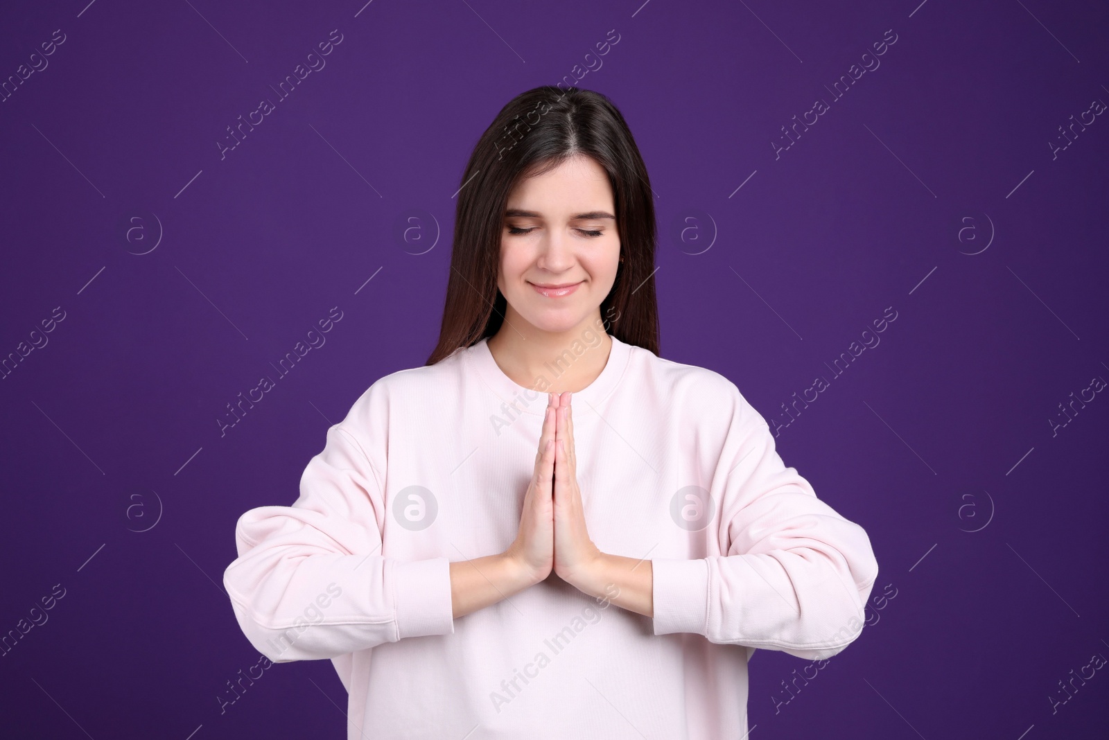 Young woman meditating on purple background. Stress relief exercise Photo of Young woman meditating on purple background. Stress relief exercise