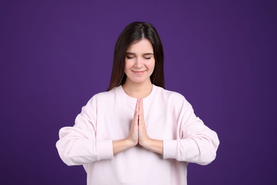 Young woman meditating on purple background. Stress relief exercise Photo of Young woman meditating on purple background. Stress relief exercise