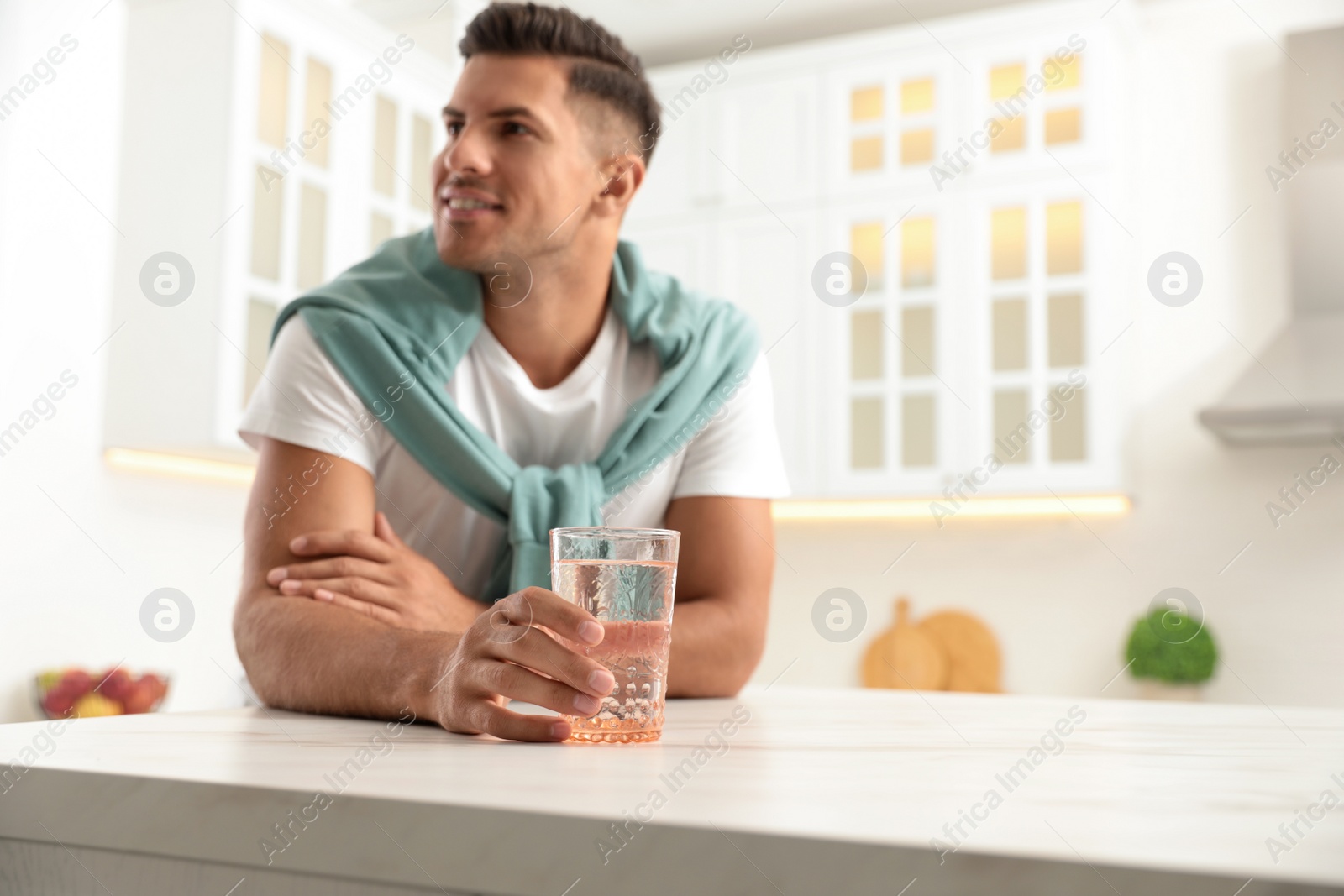 Man holding glass of pure water at table in kitchen, focus on hand Photo of Man holding glass of pure water at table in kitchen, focus on hand