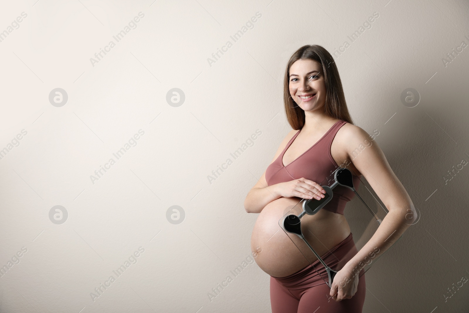 Pregnant woman with scales on beige background. Space for text Photo of Pregnant woman with scales on beige background. Space for text
