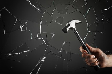 Woman breaking window with hammer on dark grey background, closeup Image of Woman breaking window with hammer on dark grey background, closeup
