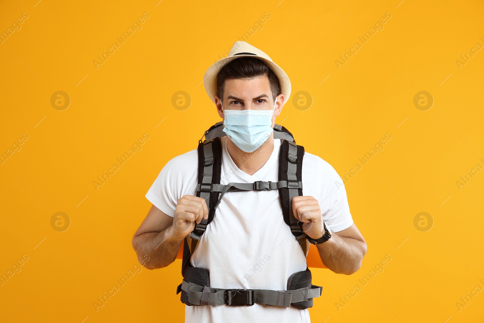 Male tourist in protective mask with travel backpack on yellow background Photo of Male tourist in protective mask with travel backpack on yellow background