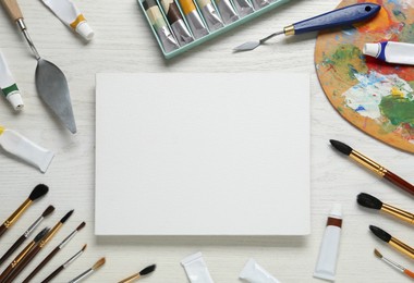 Blank canvas, tools, palette and paints on white wooden table, flat lay. Space for text Photo of Blank canvas, tools, palette and paints on white wooden table, flat lay. Space for text