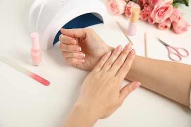 Woman doing manicure with ultraviolet nail lamp at white table, closeup Photo of Woman doing manicure with ultraviolet nail lamp at white table, closeup
