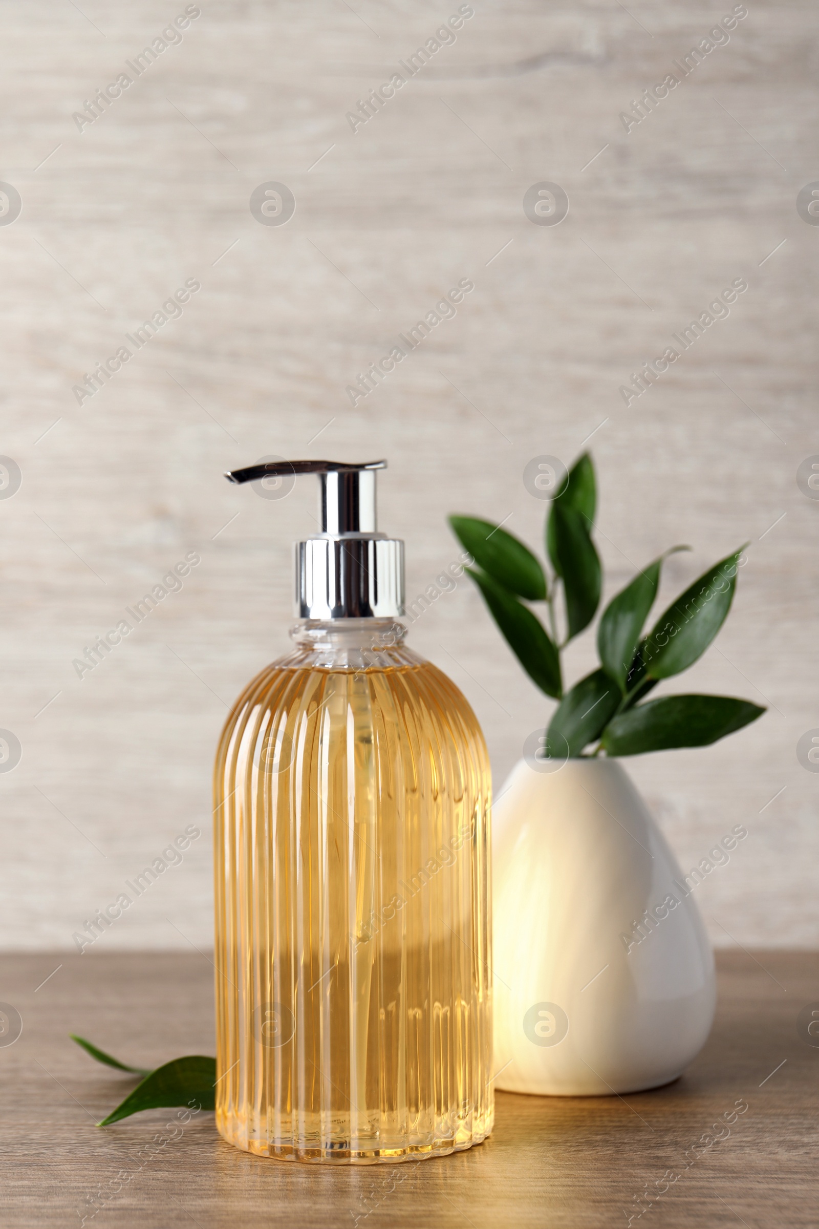 Stylish dispenser with liquid soap and green leaves in vase on wooden table Photo of Stylish dispenser with liquid soap and green leaves in vase on wooden table