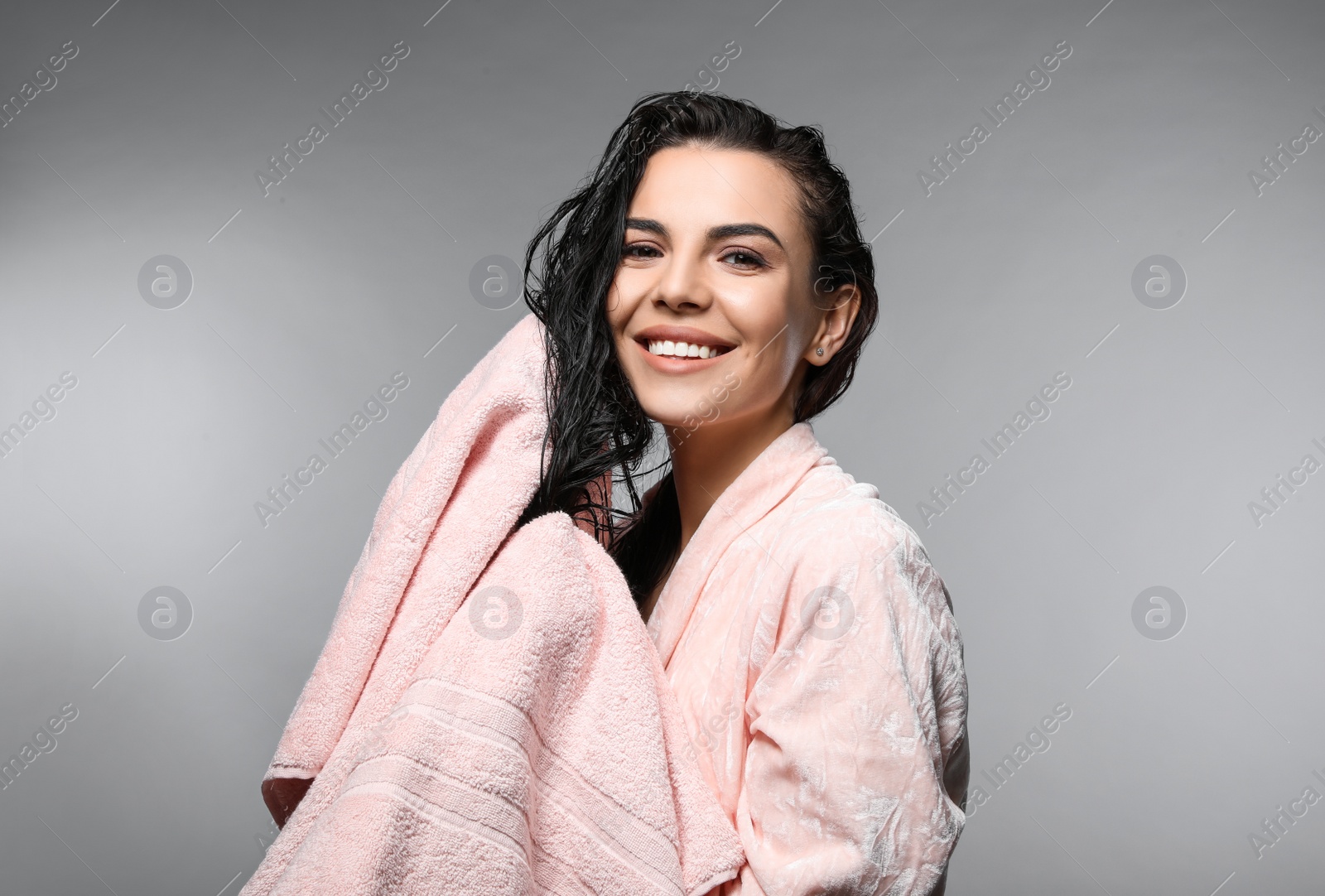 Happy young woman drying hair with towel after washing on light grey background Photo of Happy young woman drying hair with towel after washing on light grey background