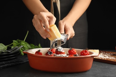 Woman grating cheese onto baked eggplant with tomatoes at black table, closeup Photo of Woman grating cheese onto baked eggplant with tomatoes at black table, closeup