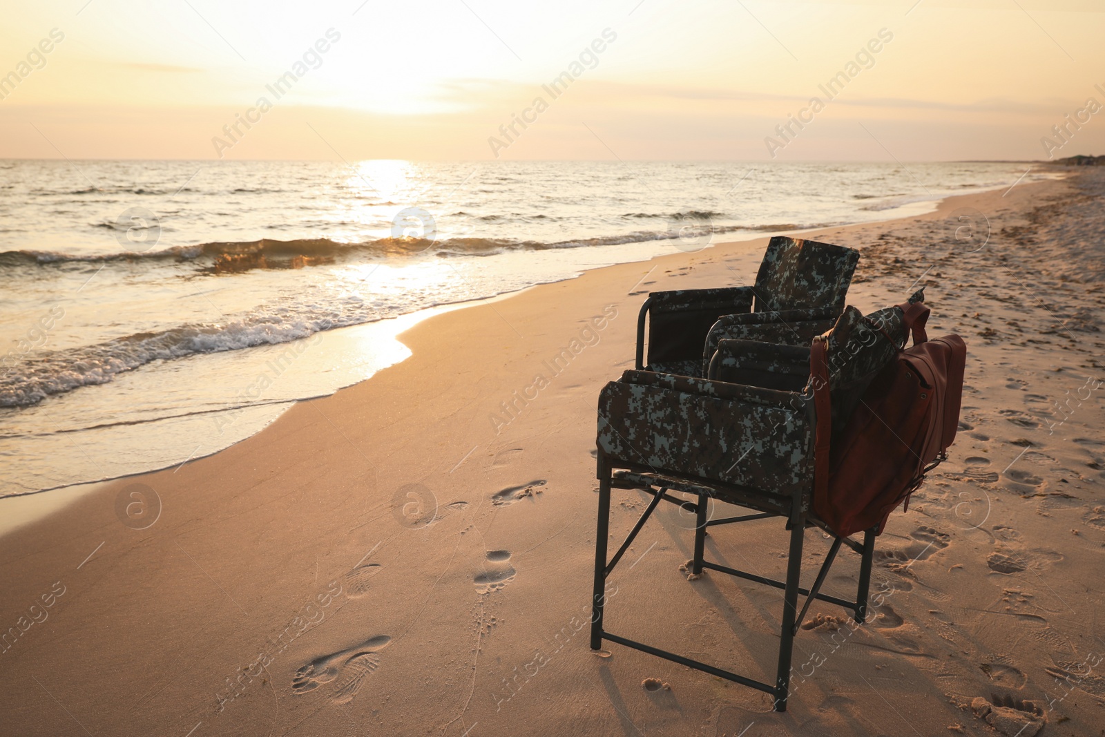 Camping chairs and backpack on sandy beach near sea, space for text Photo of Camping chairs and backpack on sandy beach near sea, space for text