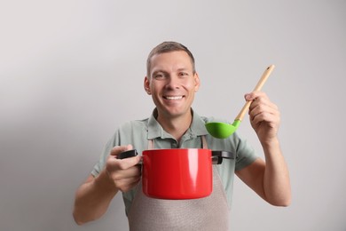 Happy man with cooking pot and ladle on light grey background Photo of Happy man with cooking pot and ladle on light grey background