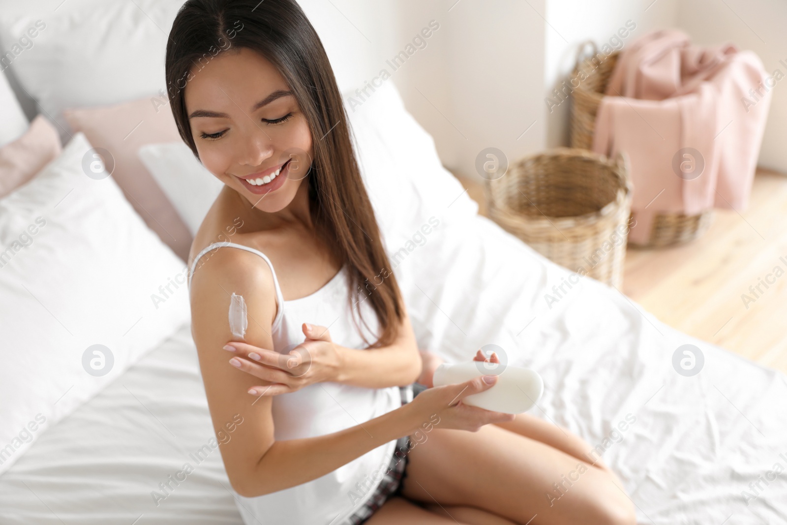 Photo of Beautiful young woman applying body cream in bedroom