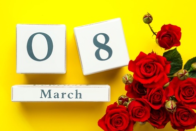 Wooden block calendar with date 8th of March and roses on yellow background, flat lay. International Women's Day Photo of Wooden block calendar with date 8th of March and roses on yellow background, flat lay. International Women's Day