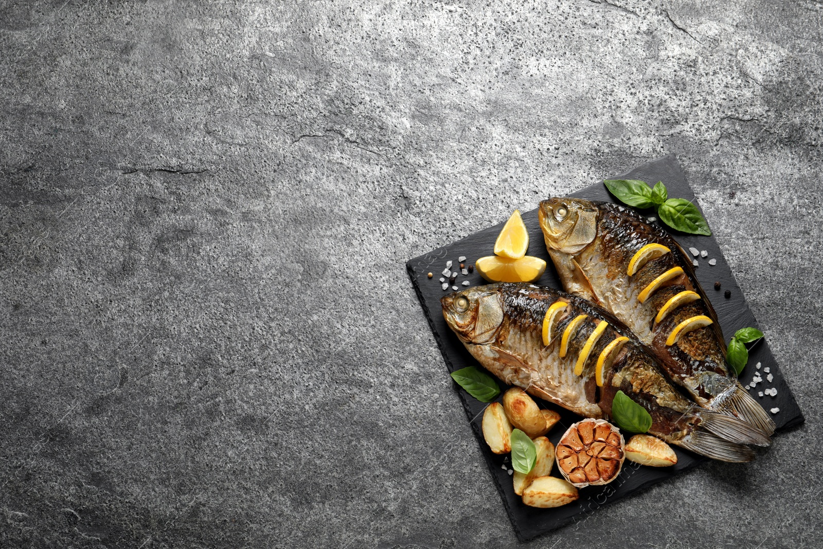 Photo of Tasty homemade roasted crucian carps served on grey table, top view and space for text. River fish