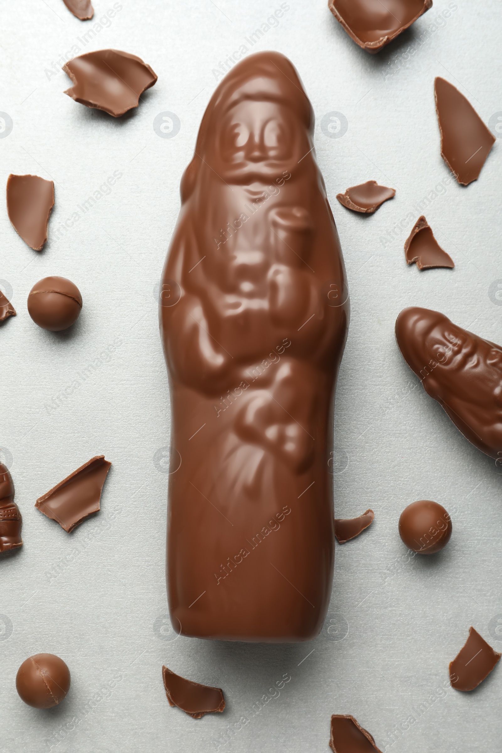 Flat lay composition with whole and broken chocolate Santa Claus candies on light grey table Photo of Flat lay composition with whole and broken chocolate Santa Claus candies on light grey table