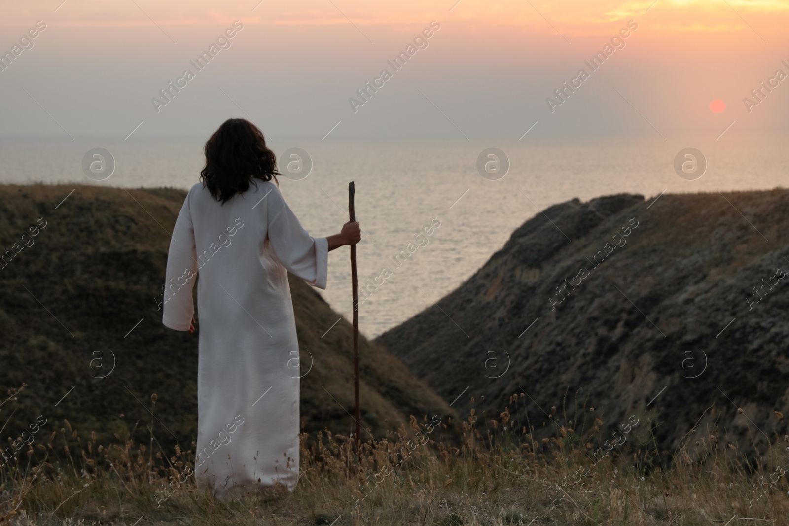 Jesus Christ with stick on hills at sunset, back view. Space for text Photo of Jesus Christ with stick on hills at sunset, back view. Space for text