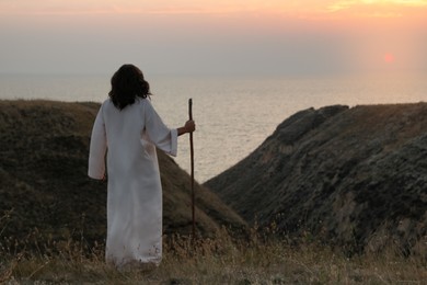 Jesus Christ with stick on hills at sunset, back view. Space for text Photo of Jesus Christ with stick on hills at sunset, back view. Space for text