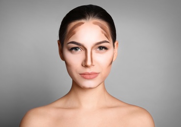 Young woman with contouring lines on her face against grey background. Professional makeup products Photo of Young woman with contouring lines on her face against grey background. Professional makeup products
